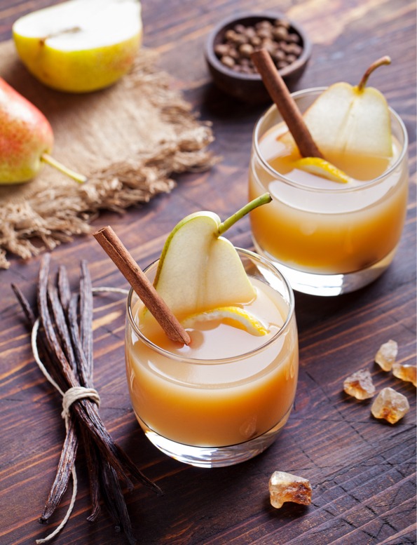 Brown liquid drink with pear, orange and cinnamon stick in glass