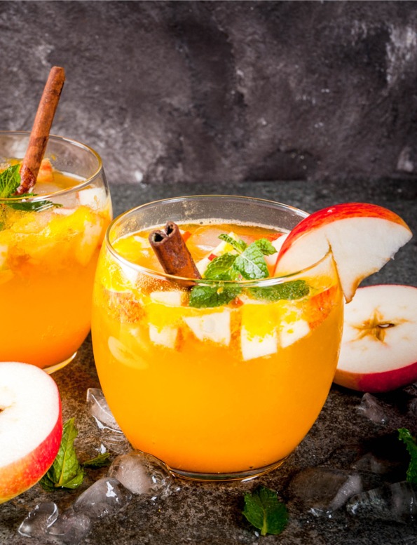 Orange liquid with apples, cinnamon and mint in glass