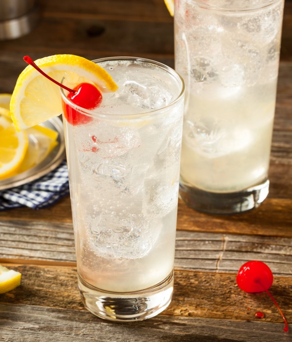 Clear liquid drink with cherry and lemon wedge in glass